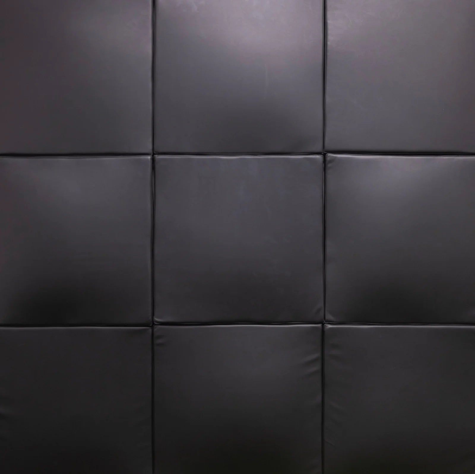 Black padded wall panels arranged in a grid pattern, showing a textured faux-leather or vinyl surface.