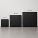Three square black upholstered panels or mats shown in increasing sizes labeled 12 x 12 inches, 20 x 20 inches, and 24 x 24 inches, against a light gray wall and concrete floor.